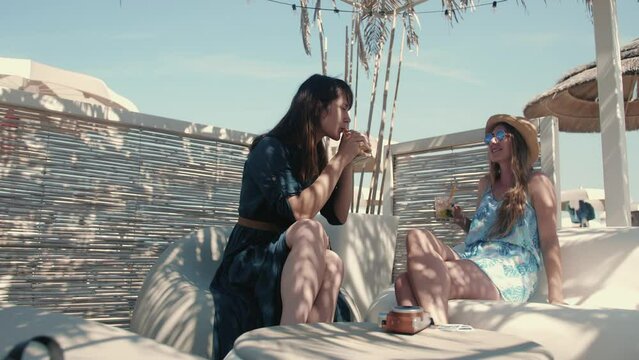 Girls vacation. Two attractive female friends talk in a beach bar, while enjoying cocktails.