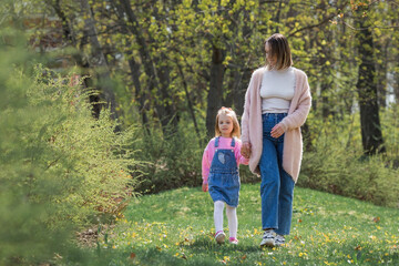 Fototapeta premium A beautiful little girl in pink clothes walks with her mother in the park in the fresh air. Family, children, motherhood.