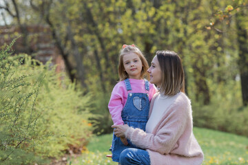 Fototapeta premium A beautiful little girl in pink clothes walks with her mother in the park in the fresh air. Family, children, motherhood.