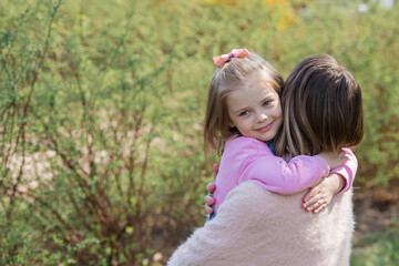 A beautiful little girl in pink clothes walks with her mother in the park in the fresh air. The child hugs his mother. Family, love, children, motherhood.