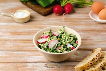 Spring salad of wild garlic, radish and boiled eggs in a ceramic bowl on a wooden background. The use of wild plants for food, the first spring greens.