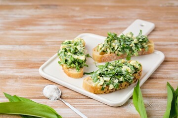 Open sandwiches with spring salad of wild garlic and boiled eggs on a white ceramic board on a wooden background. Using wild plants for food