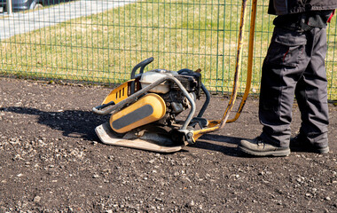 Close up view of home owner use plate compactor tool to build parking lot with recycled asphalt chips in home garden outdoors in spring.