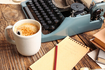 Cup of coffee with notebook and typewriter on wooden table, closeup