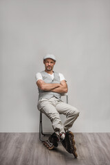 Smiling young man wearing gray west and cap sitting on chair in roller skates