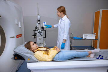 Little patient lying on long medical table during MRI scan procedure in hospital.