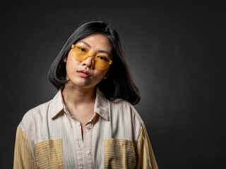 A portrait of an Asian girl wearing yellow glasses with a casual fashion style posing with a hip...