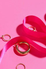 Stylish rings with ribbon on pink background, closeup