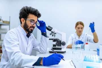 Health care researchers working in science laboratory microscoping making notes of his investigation
