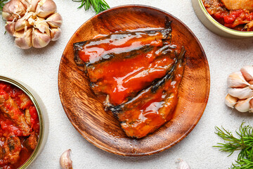 Composition with canned fish in tomato sauce, dill and garlic on white table