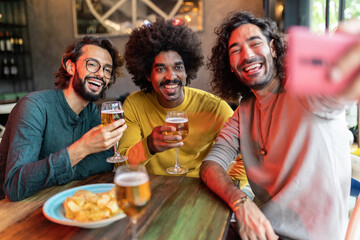 Group of mixed race young male friends taking selfie portrait while drinking cold beer in a bar