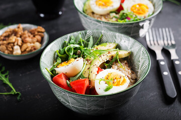 Breakfast oatmeal porridge with boiled eggs, avocado, tomatoes and green herbs. Healthy balanced food.