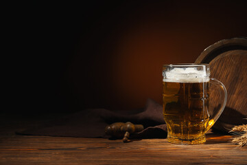 Mug of cold beer and wooden barrel on table against dark background