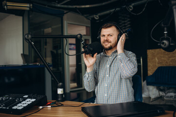 Handsome happy young male radio host broadcasting in studio, using microphone and headphones.