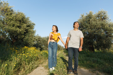 Outdoor shot of young couple in love walking on pathway through grass field. Man and woman walking along grass field.