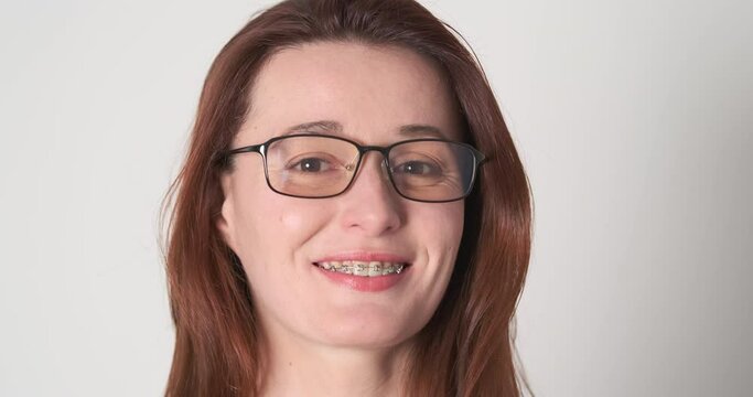 Confident young woman wearing glasses, smiling, has metal braces on her teeth. Close-up, portrait. Concept of orthodontist services, dentistry.