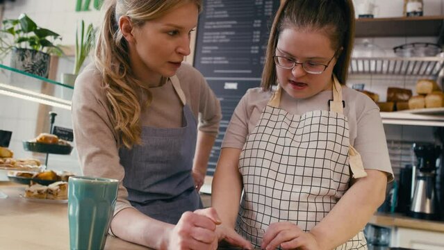 Down syndrome girl browsing phone together with her workmate in the cafe. Shot with RED helium camera in 8K. 