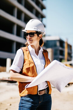 On a sunny day, a 32-year-old civil engineer/architect, clad in a white shirt and hard hat, confidently holds building plans at construction site, embodying ambition in this portrait. Generative AI