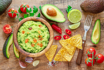 Guacamole, guacamole ingredients and chips on wooden background.  Flat lay.