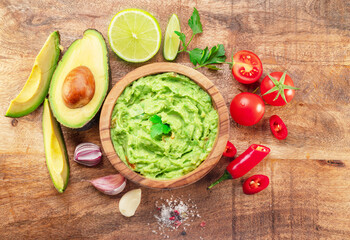 Guacamole, guacamole ingredients and chips on wooden background.  Flat lay.