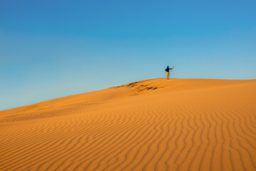 Fototapeta na wymiar Young male standing on the top of sand dune . Travel concept. Desert adventure.