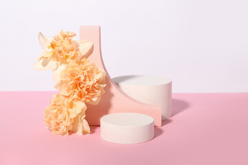 Decorative plaster podiums with flowers on pink table against white background