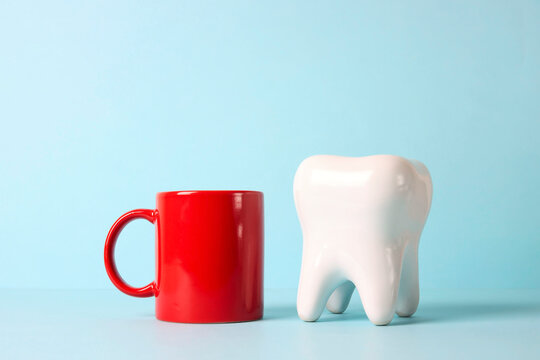 White human tooth with a red mug of coffee or tea. Dental care concept.