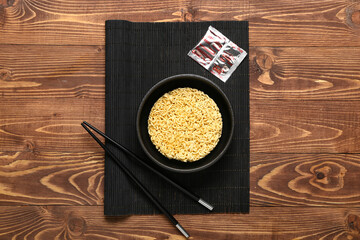 Bowl of instant noodles, chopsticks, seasoning and bamboo mat on wooden background