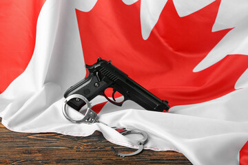 Flag of Canada with gun and handcuffs on wooden background