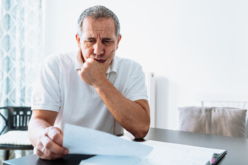 middle-aged man at table at home reading bill or letter