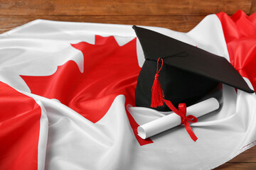 Graduation hat with diploma and flag of Canada on wooden background, closeup