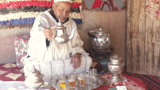 Moroccan senior man in traditional dress serving mint tea with silver utensils on terrace