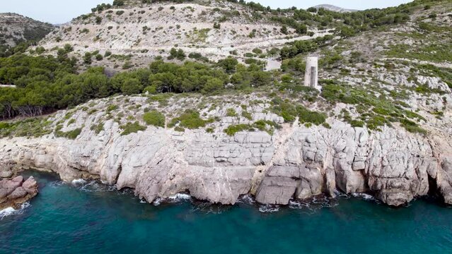 Lateral top view of a rocky coastline defensive medieval tower among turquoise Mediterranean Sea, Oropesa del Mar, Spain