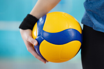 Volleyball ball in hands of a female player standing in gym. Close up of ball in hands of a learner, training, mastering skills concept