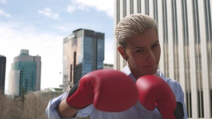Businesswoman throwing punches wearing red boxing gloves outdoors - Powered by Adobe