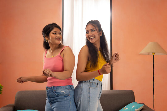 Two young women dancing together in living room
