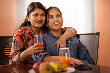 Two young women watching TV together as they sit on a dining table