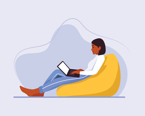 dark-skinned girl with short hair sits on a bean bag chair with a laptop