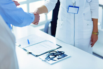 Female doctor handshaking a patient's hand and smiling. - 596630212
