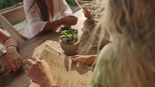 Woman reading restaurant menu close-up. Female hands holding menu in outdoor cafe turning pages choosing food and drinks lit by the sun. Picking refreshers and beverages. Selecting appetizers