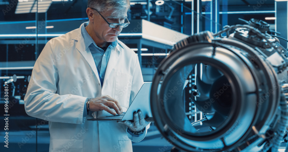 Poster middle aged industrial engineer working on a futuristic jet engine, standing with laptop computer in