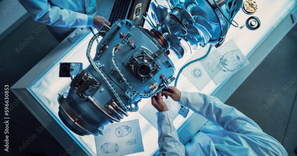 Aufkleber Top Down View of Two Engineers Discussing Work, Talking, Using Laptop Computer and Checking Blueprints in Jet Motor Manufacturing Facility. Scientists Researching Innovative Turbine Engine