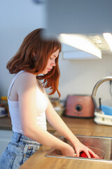 Girl with red hair wash apples in the kitchen. 