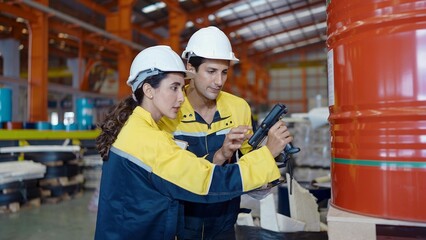 Two factory workers man and woman in uniform using barcode scaner scan product to checking stock at industrial warehouse