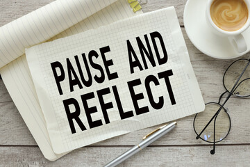 pause and reflect On a wooden background, a notepad with text with a cup of coffee and glasses