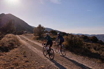 Gravel adventure..Back view of professional gravel cyclists riding uphill with mountain view at sunset. Alicante region in Spain 