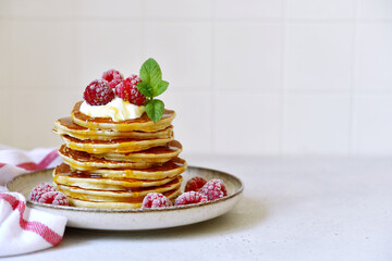 Delicious homemade pancakes with whipped cream, maple syrup and raspberry for a breakfast.