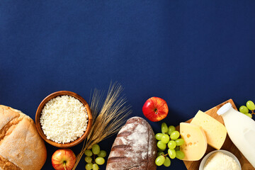 Jewish holiday Shavuot concept. Flat lay cottage cheese, bottle of milk, cereal bread, grape, apples, wheat on blue background. - obrazy, fototapety, plakaty