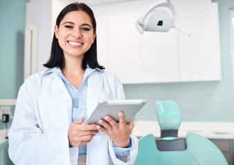 Young female caucasian dentist wearing a labcoat and smiling while using a digital tablet in her...