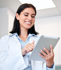 A confident, young female dentist working on her digital tablet in the doctors room. A beautiful...